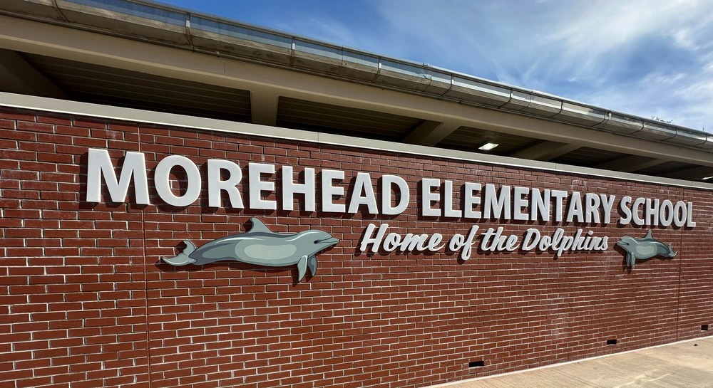 Image of a brick wall with a sign that reads Morehead Elementary School Home of the Dolphins with 2 dolphin icons on either side of the sign.