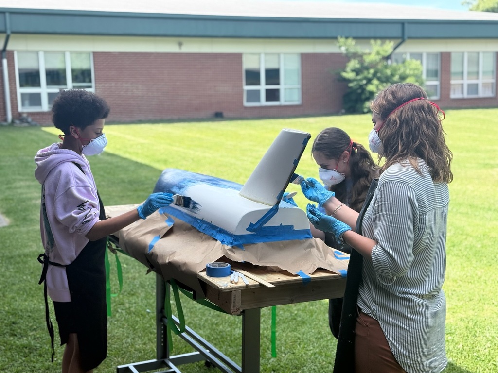 Students with masks painting a boat outside