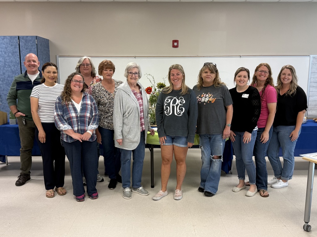 Image of Newport Elementary School volunteers who were celebrated at today's volunteer breakfast, 11 people in all standing in front of a table with flowers
