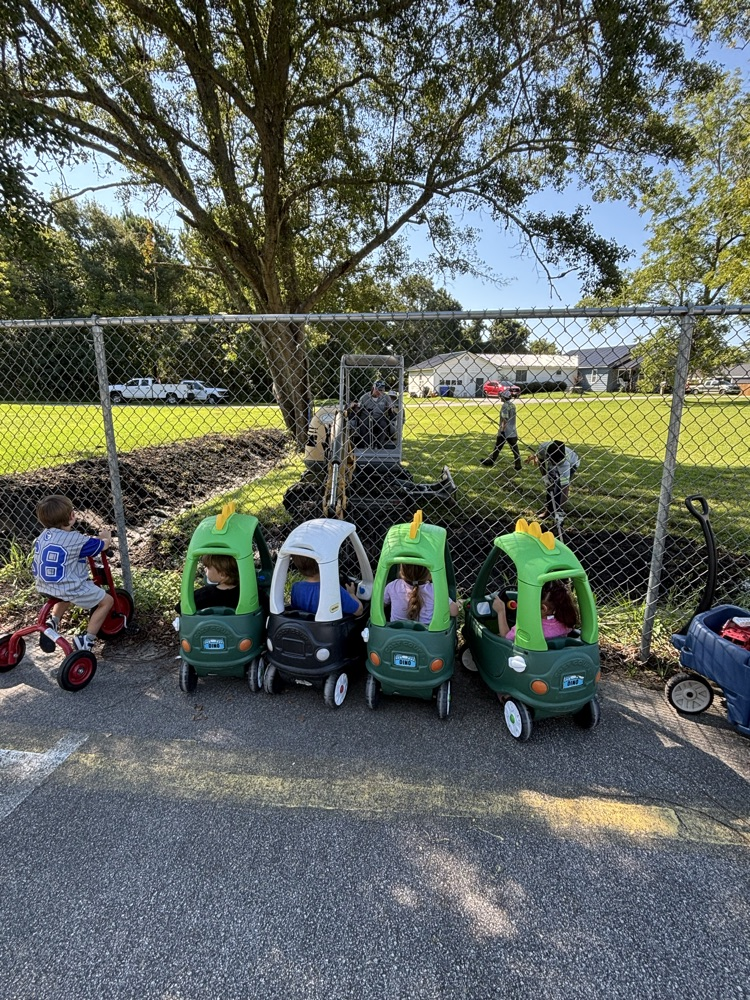 line up of children in toy cars watching bulldozer work