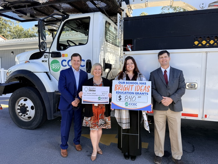 picture of four people in front of a power truck with one person receiving a grant check