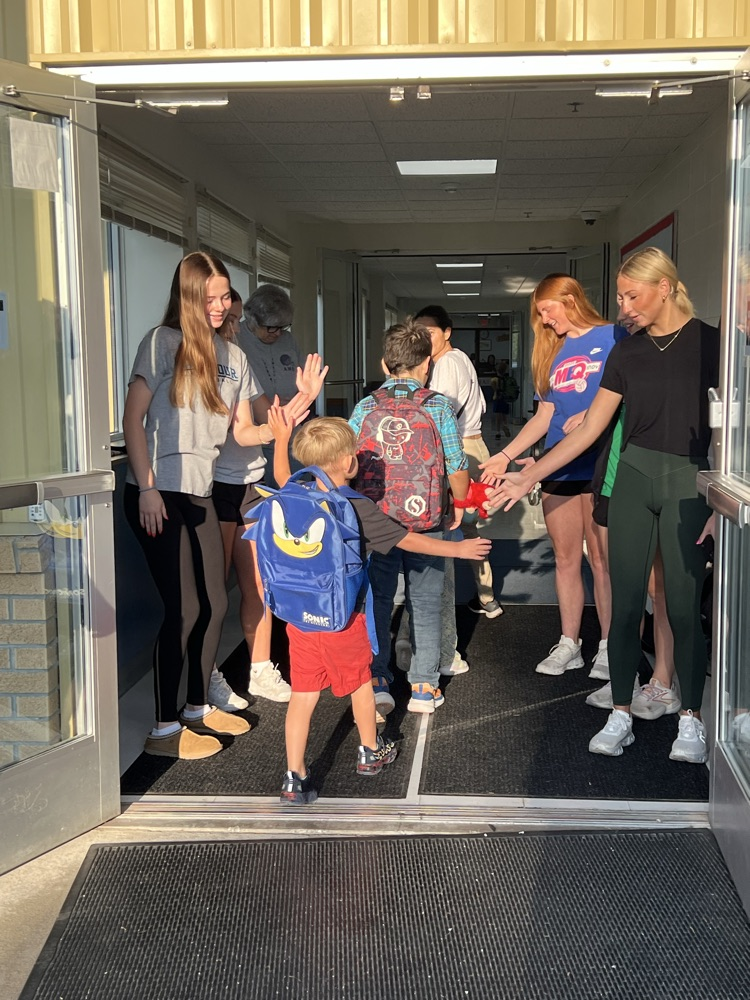 high school students giving elementary students high fives as they enter the school building  