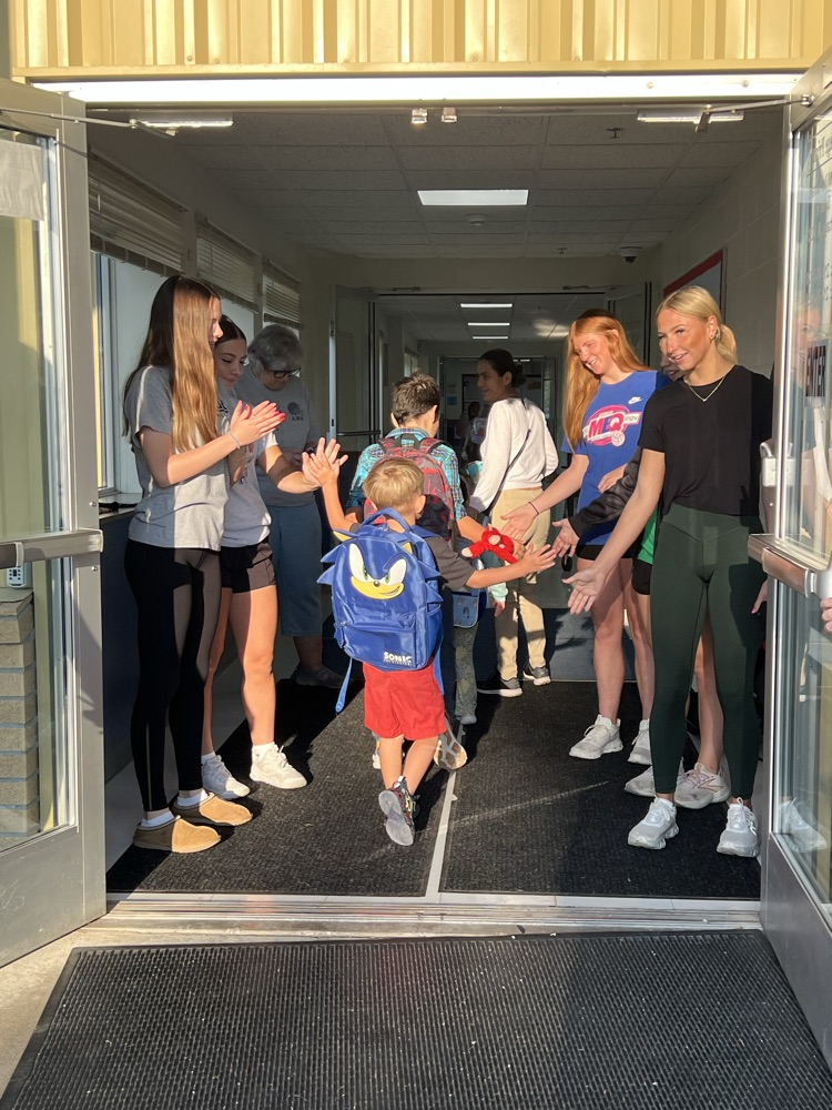 high school students giving elementary students high fives as they enter the school building