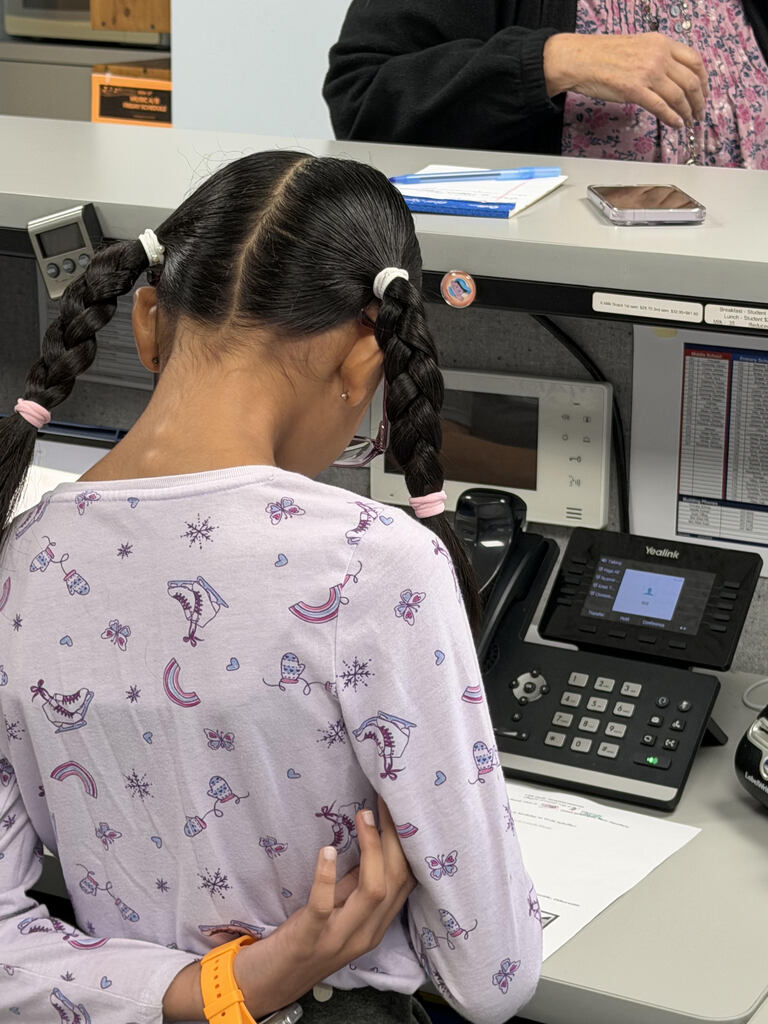 student standing by phone with her back to the camera reading the morning announcements