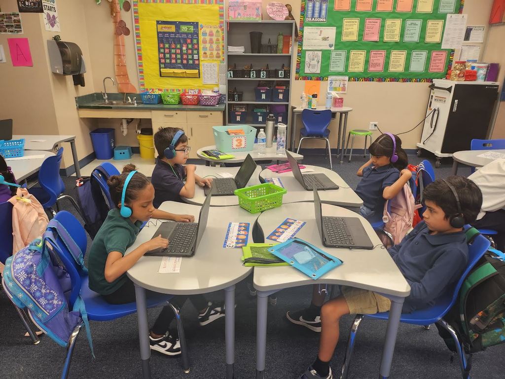 A group of second graders using laptops and wearing headphones.