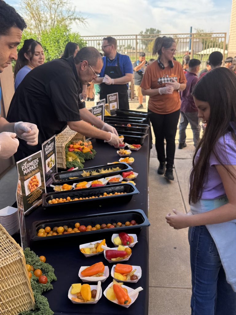 Table full of sunfruit, golden berries, and peppers. Workers handing them out to students.