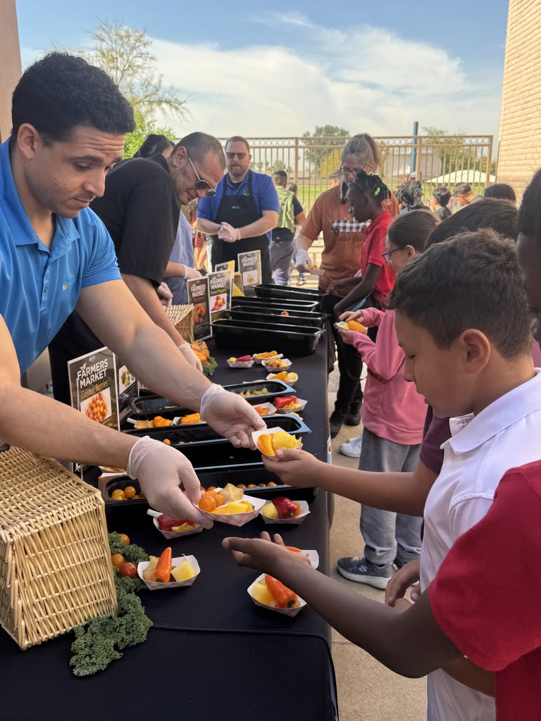 Table full of sunfruit, golden berries, and peppers. Workers handing them out to students.