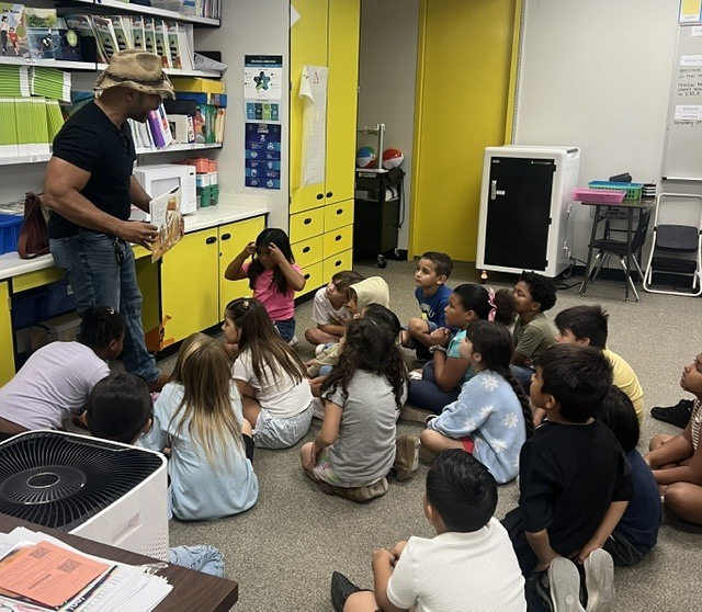 A volunteer reader reads a book to a class.