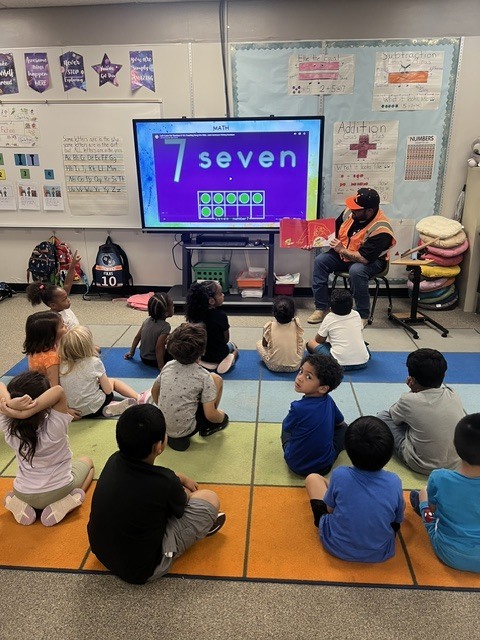 A volunteer reader reads a book to a class.