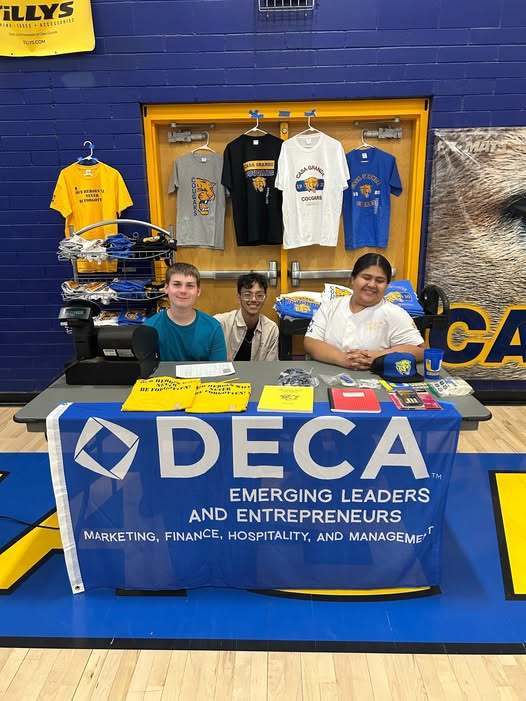 three students sitting at a table decorated with DECA Marketing items for sale @ Back To School Roundup