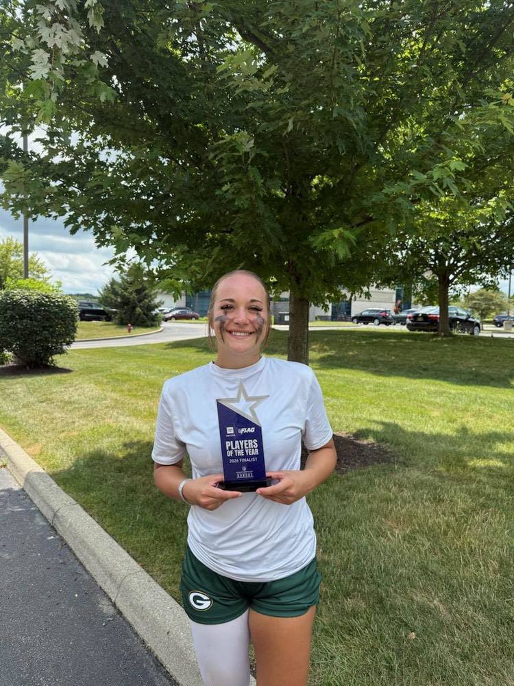Kayla Tucker standing on green grass by a green tree in soccer uniform holding a trophy