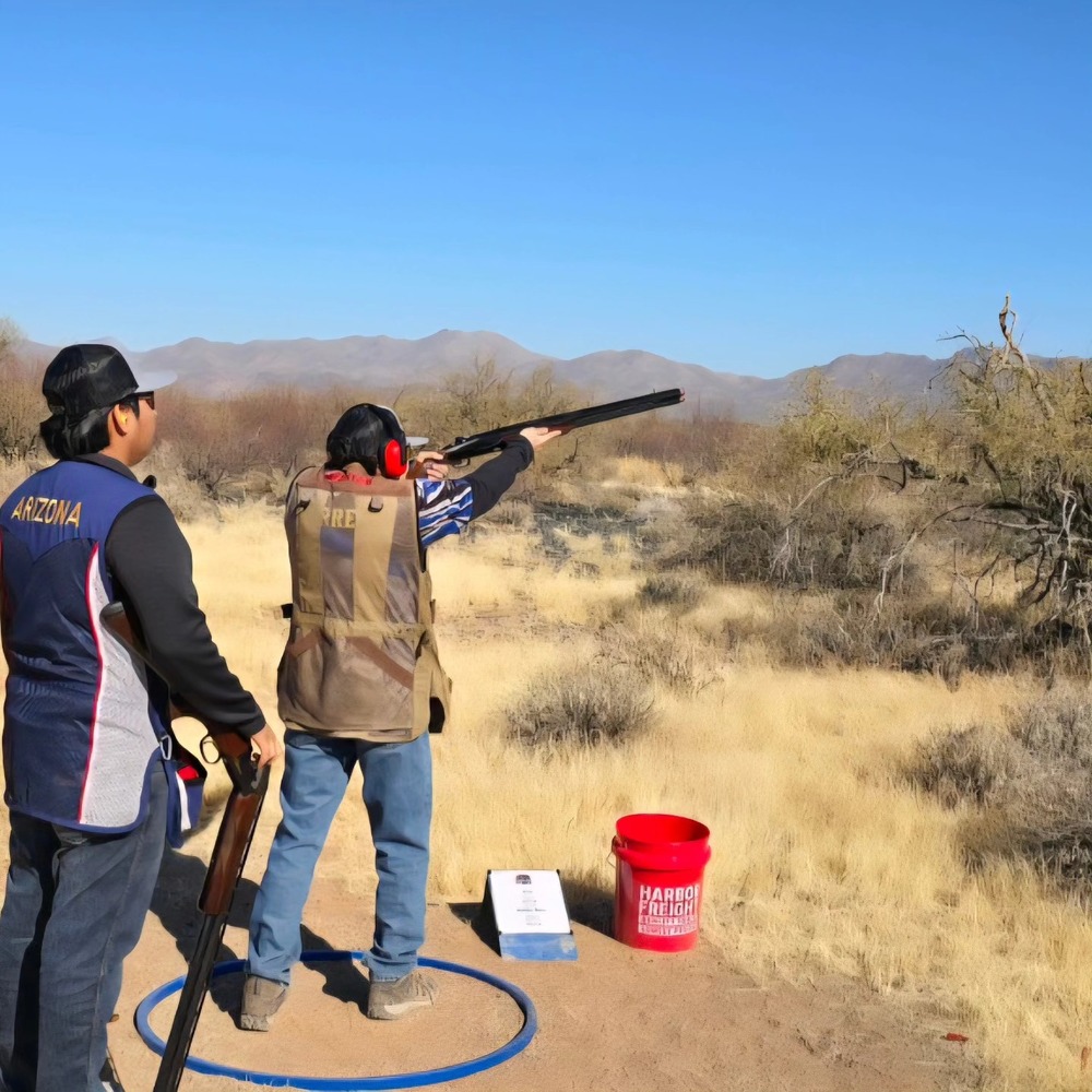 Trap & Skeet Club student shooting a gun with a person standing behind