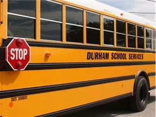 side of bus with stop sign and words "Durham School Services" printed on the side of the bus