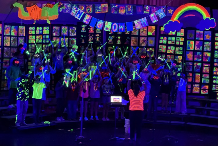 students sing and tap glow sticks under black light at the glow concert