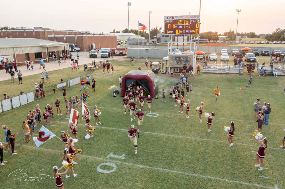 Football team running on field with cheer leaders