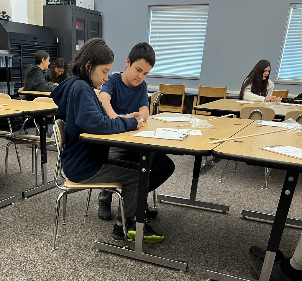 Two students building a catapult out of popsicle sticks and rubber bands.