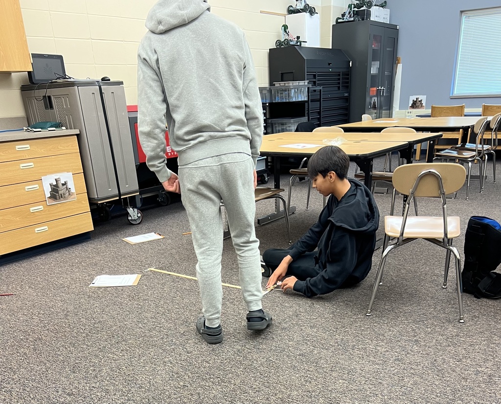A student watching his partner launch a candy pumpkin with a popsicle stick catapult.
