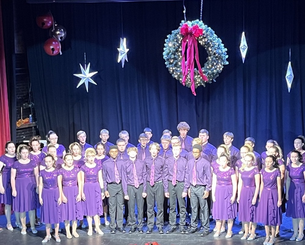 Choir Students dressed in purple standing on a stage with christmas wreath and stars