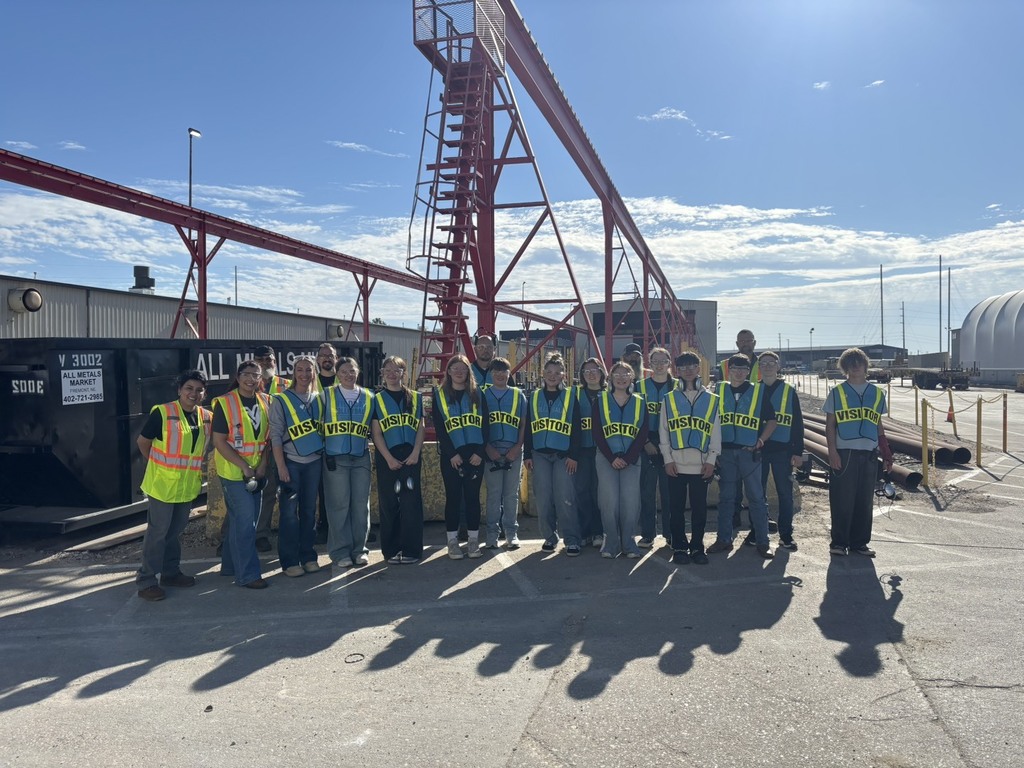 Twelve students, one teacher, and two workers all in safety vests posed for group picture outdoors