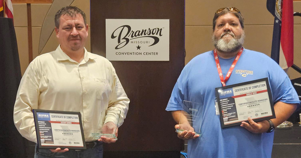 Man in cream button up shirt stands next to Branson Convention Center sign  next to man in blue t-shirt.