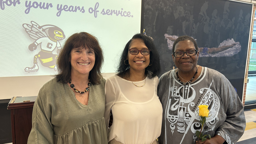 Three women stand together, smiling at the camera.