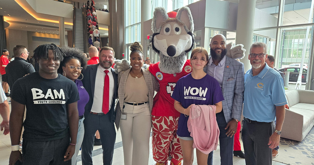Row of people, smiling, stand next to Kansas City Chiefs wolf mascot.