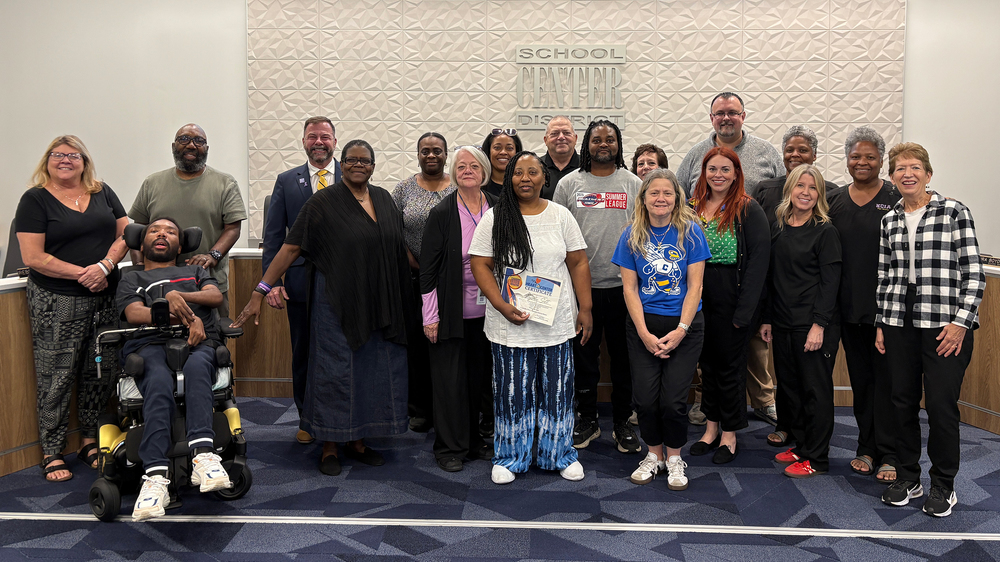 Large group of people stand in front of Center School District sign.