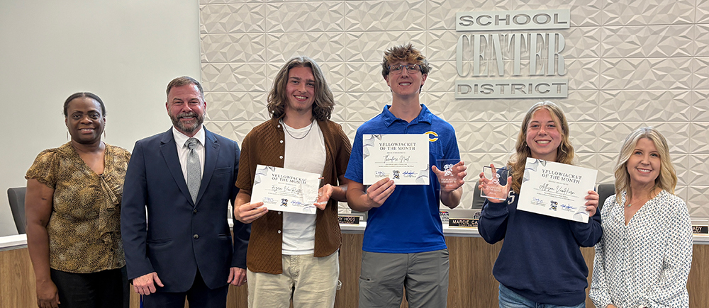 Six people stand smiling in front of Center School District sign..