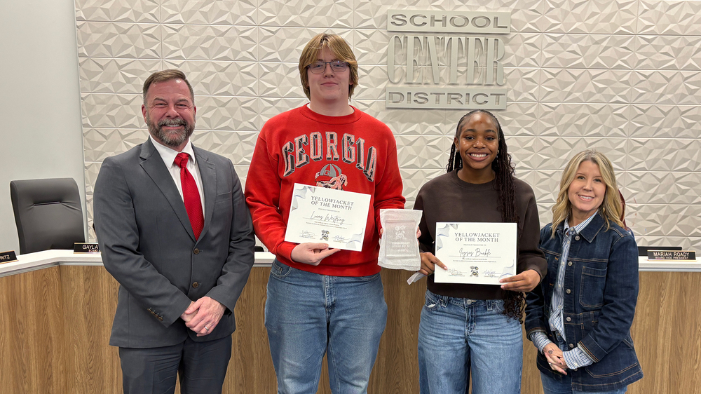 Superintendent Troy Hogg, CHS student Lucas Westring, CHS student Icysis Buckle, and Board Chair Marcie Calvin smile in front of the board dias.
