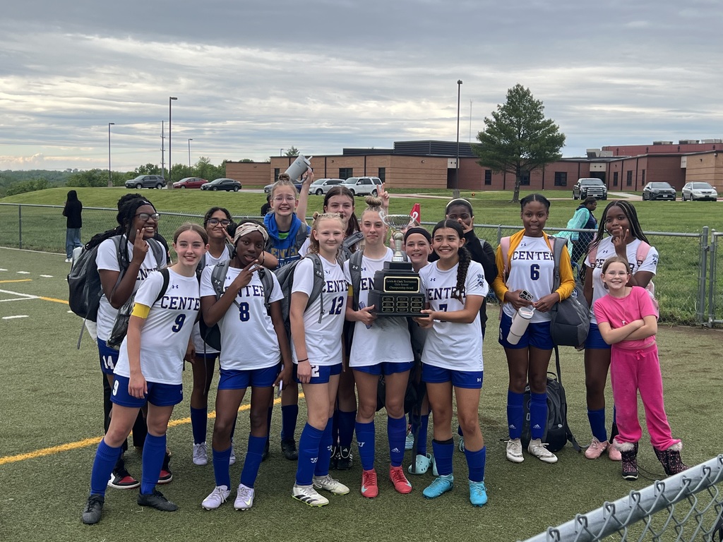 The girls soccer team proudly poses together, holding their trophy after winning the championship.