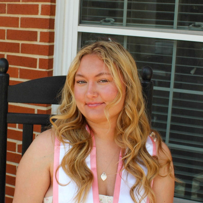 Woman with long blonde hair sits in black rocking chair in front of a brick wall.