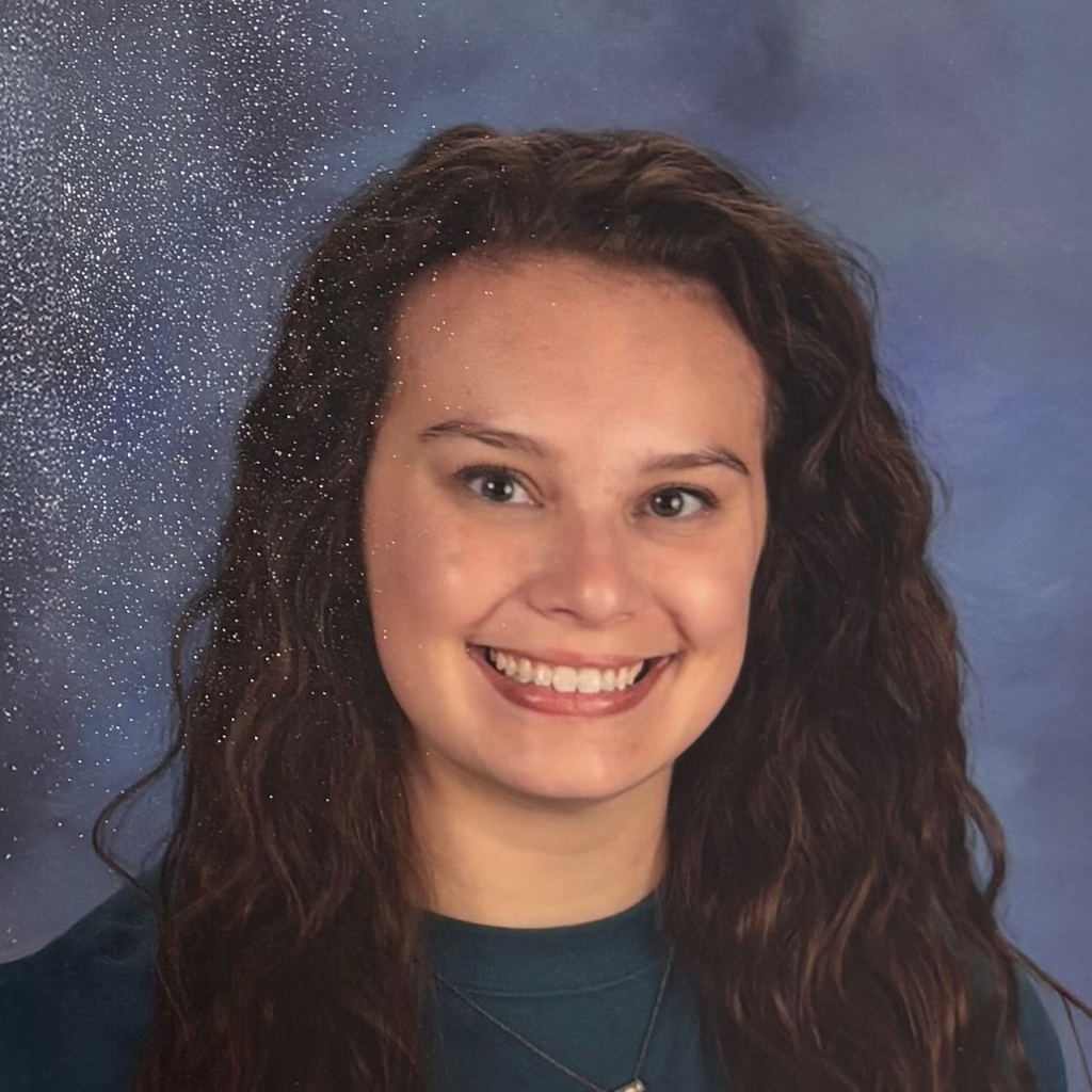 Woman with brown curly hair, and teal shirt smiles in front of a blue marbled background.