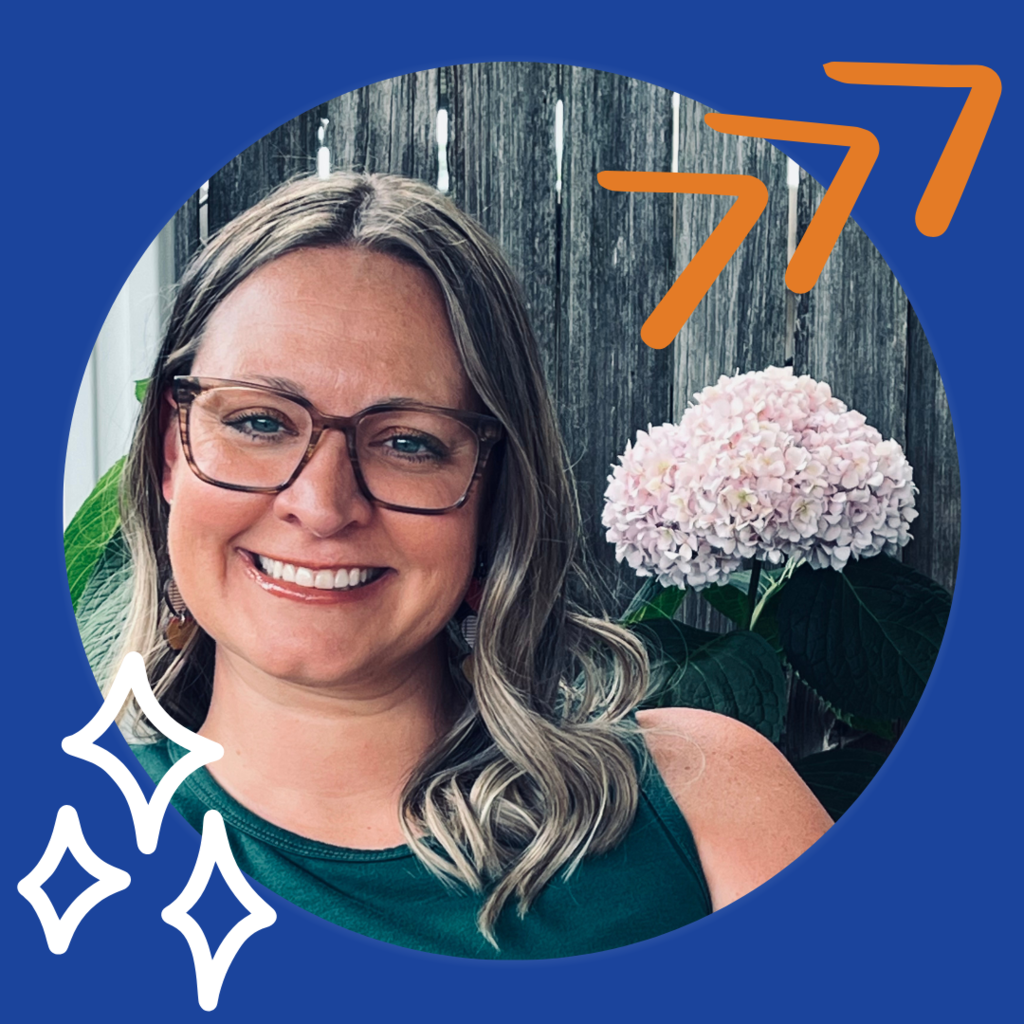 Woman with blonde hair and glasses with a green tank top and pink flower over her shoulder.