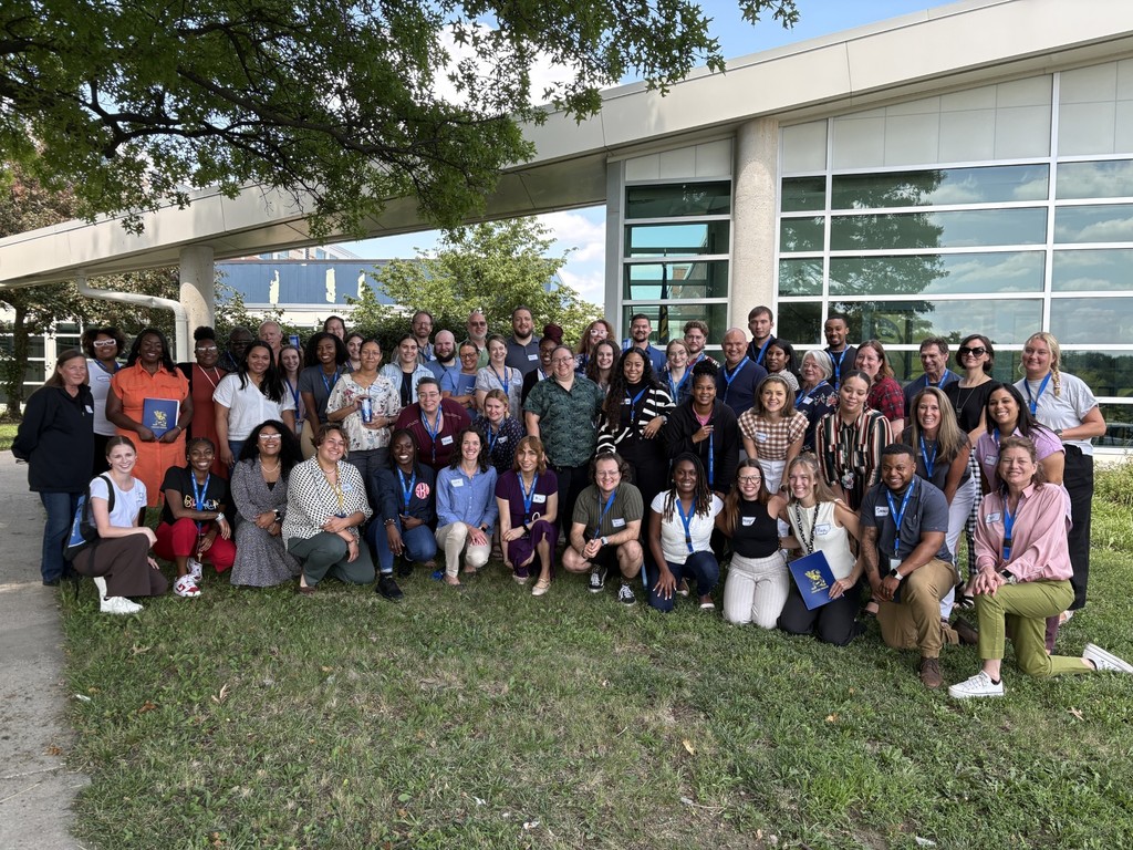 Staff stand in rows outside in front of a building with glass windows.