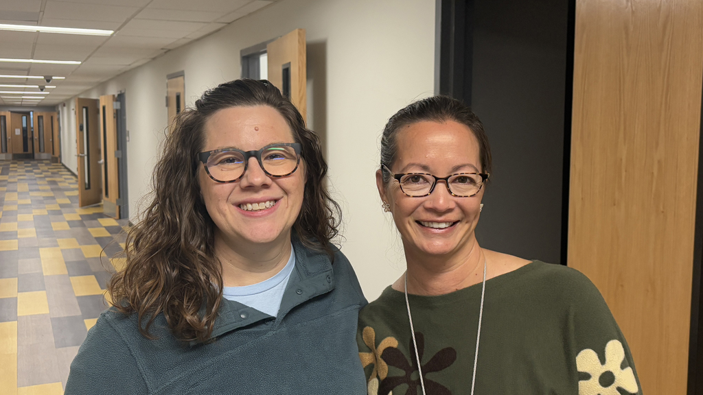 Two school psychologists stand smiling in a hallway.