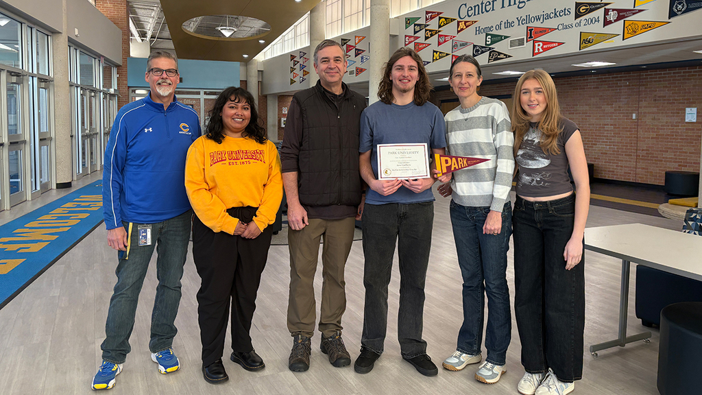 Ezra Van Riette, his parents, sister, and Principal Mark Wiegers, stand in front of the college pennants at Center High School, with a scholarship representative from Park University.