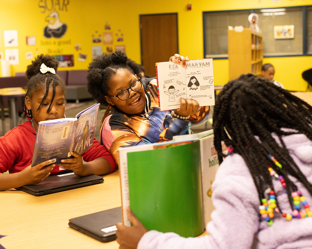 Three kids sit at a table with books in their hands.