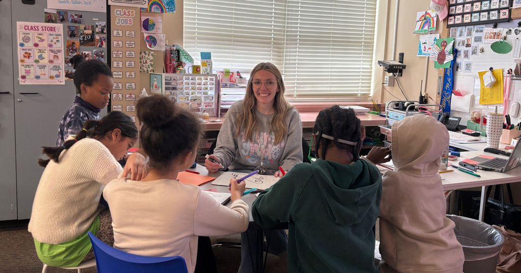 Fourth grade teacher Ms. Kylie Warner sits at a table with five of her students.