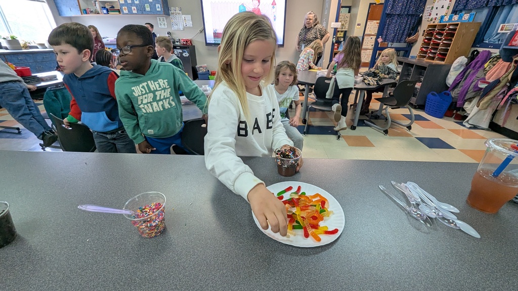 Kindergartener adding gummy worms to their "dirt cup"