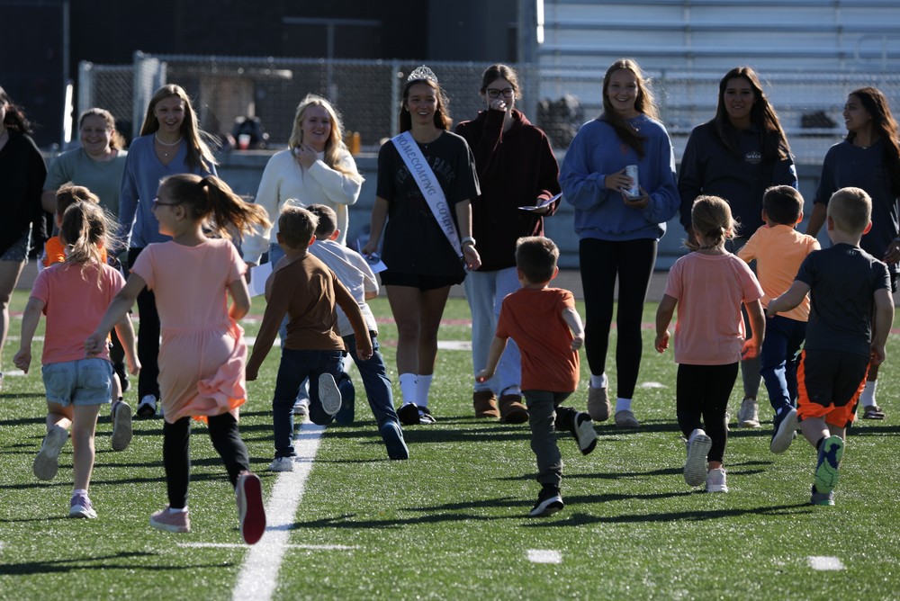 Kindergarten students running towards seniors on the football field