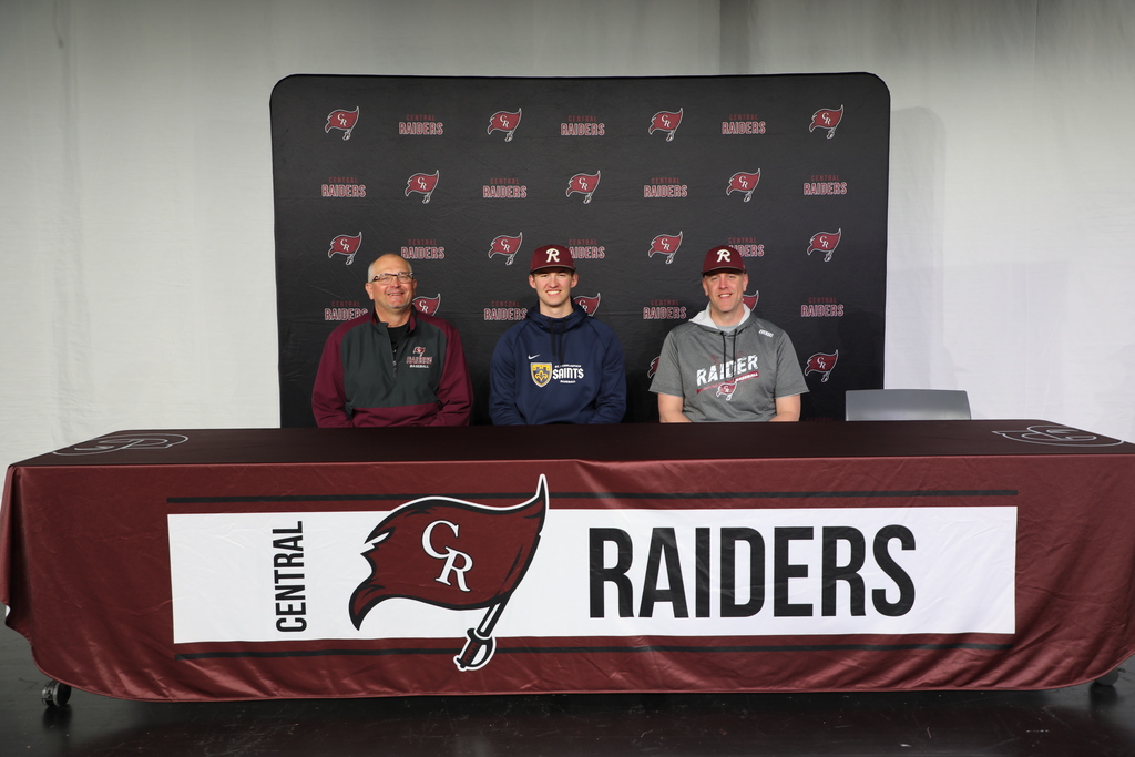 A student sitting with their coaches signing a college scholarship