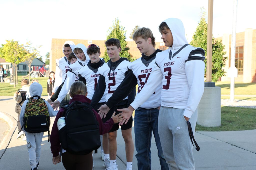 Senior football players high fiving elementary students as they get off the bus