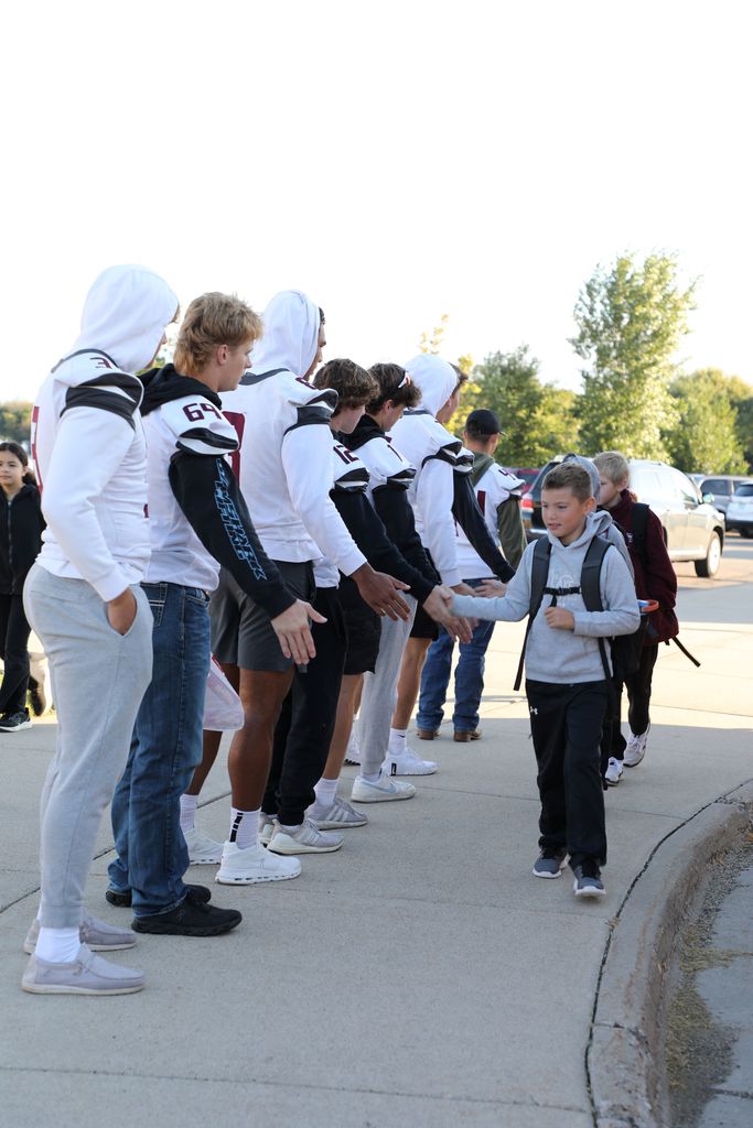 Senior football players high fiving elementary students as they get off the bus