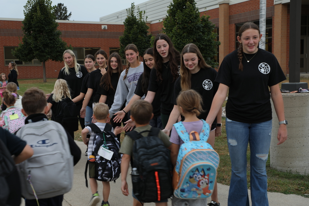 varsity volleyball players greeting elementary students as they get off the bus