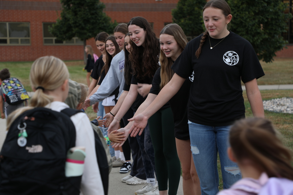 varsity volleyball players greeting elementary students as they get off the bus