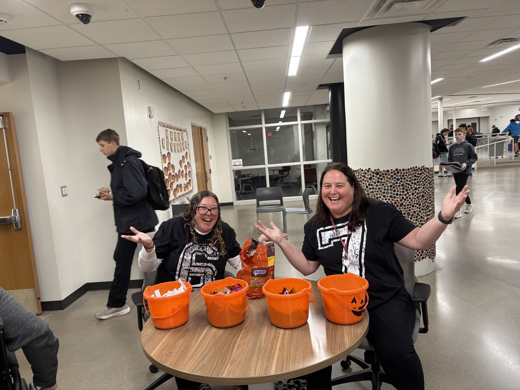 Two teachers making a silly pose and handing out candy and inspirational messages. 