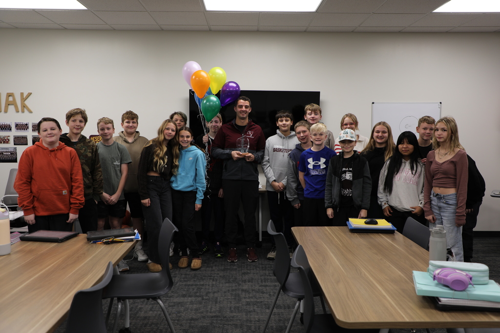 A teacher standing with a group of students , holding a plaque for being nominated for teacher of the year. 