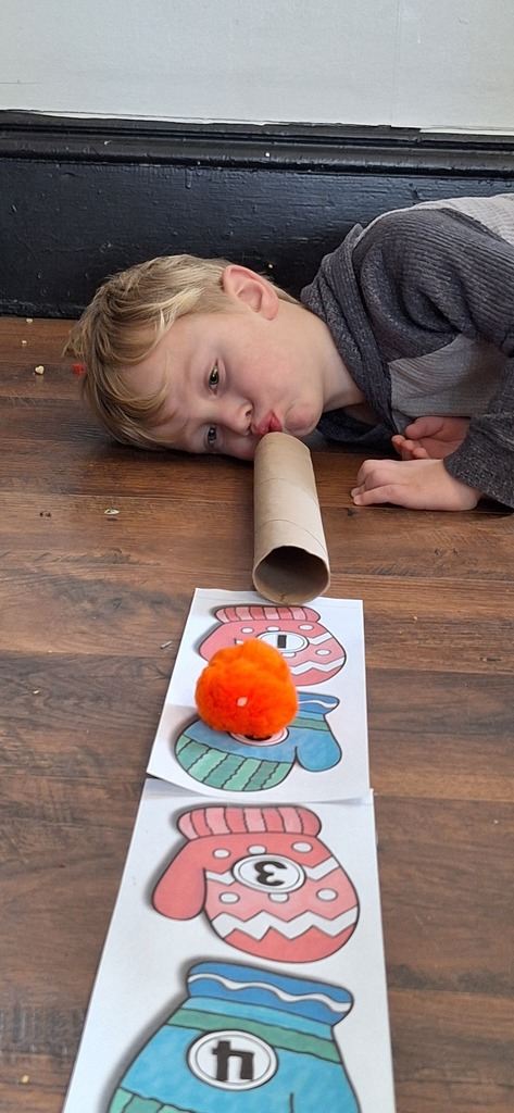 student blowing pom pom through tube