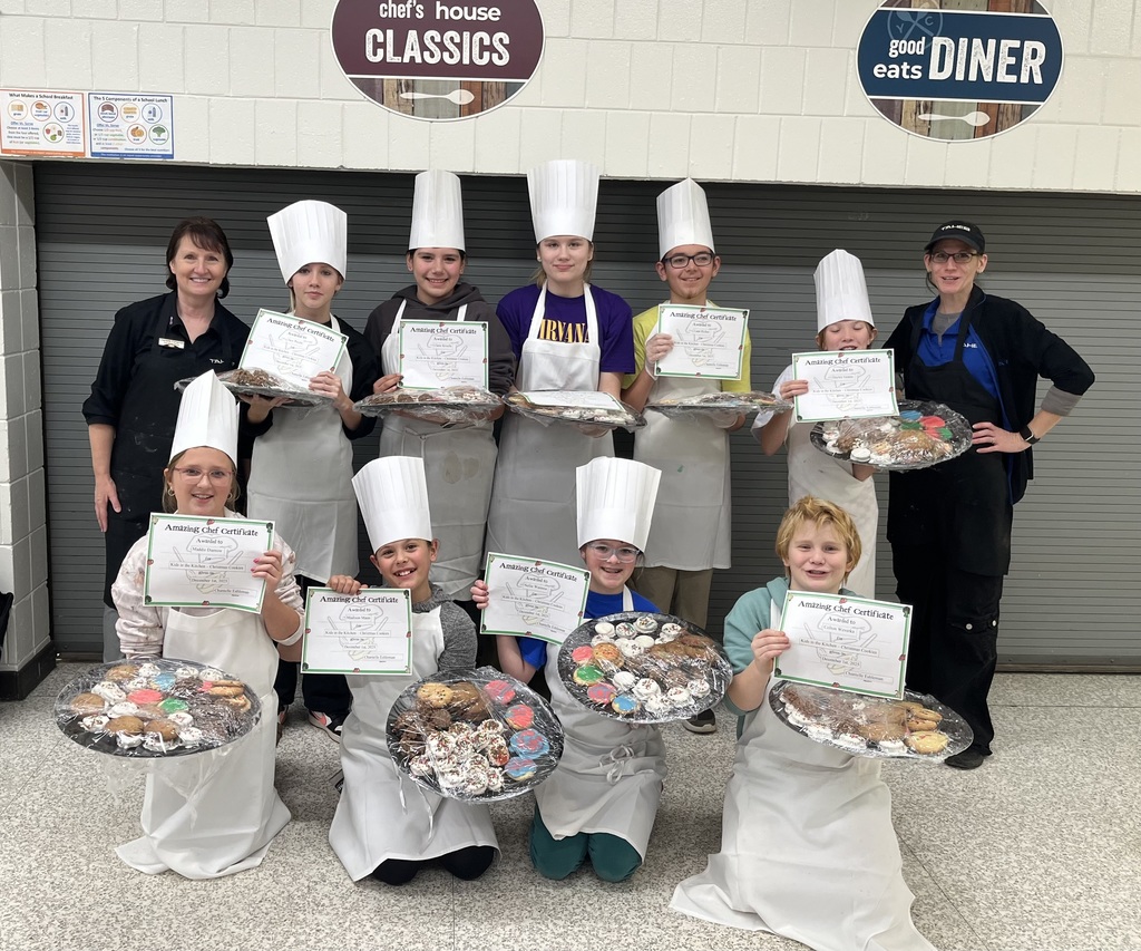 students holding trays of cookies and certificates, wearing chef hats