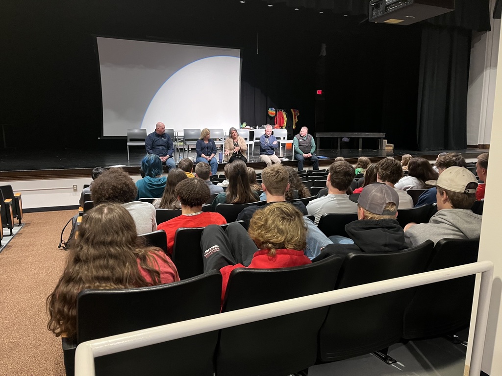 panel of speakers on auditorium stage in front of high school students